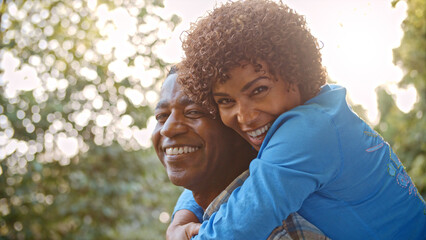 Outdoor Portrait Of Mature Couple With Woman Hugging Man From Behind With Lens Flare