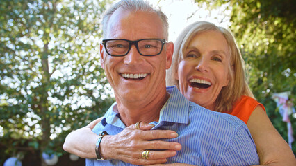 Outdoor Portrait Of Mature Couple With Woman Hugging Man From Behind With Lens Flare