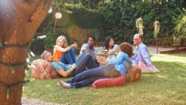 Group Of Smiling Mature Friends Enjoying Drinks And Snacks In Backyard Garden Together - Powered by Adobe