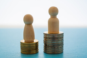 Concept of unequal pay in the workplace between men and women. Wooden figures on piles of coins.