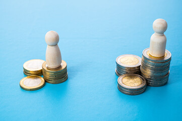 Concept of unequal pay in the workplace between men and women. Wooden figures on piles of coins.