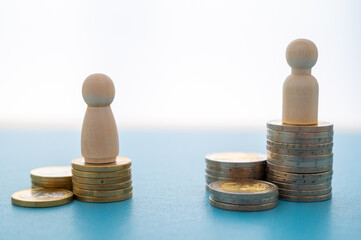Concept of unequal pay in the workplace between men and women. Wooden figures on piles of coins.