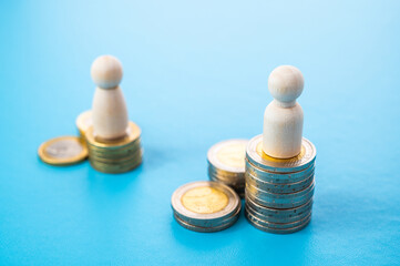 Concept of unequal pay in the workplace between men and women. Wooden figures on piles of coins.