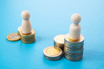 Concept of unequal pay in the workplace between men and women. Wooden figures on piles of coins.