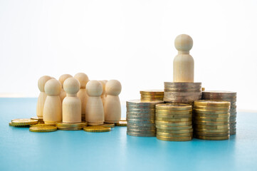 Wooden figures, on piles of coins, concept of wealth distribution. Few people hold most of the wealth.
