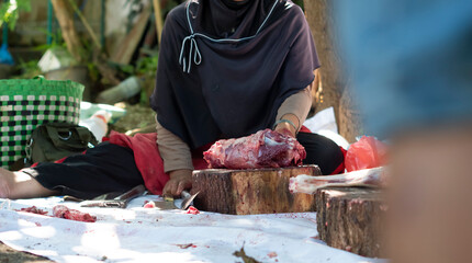 A group of women are cutting a pile of goat meat on a wooden tray with a knife during the Eid al-Adha celebration.  The butcher cuts raw goat meat with a knife. Ied al adha concept.