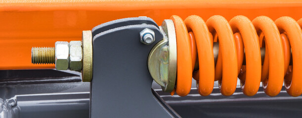 Orange hard spring made of steel. Part of big industrial or agricultural machine