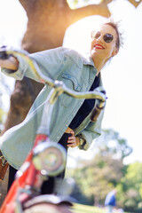 Portrait young adult pretty woman with red vintage retro bike and pin-up casual outfit green city park bright sunny summer day. Happy beautiful female person cycling outdoors. Healthy lifestyle