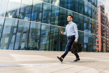 Businessman Confidently Strolling With a Tablet, Enjoying a Sunny Day in a Modern Urban Environment...