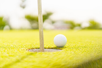 Golf ball resting near the hole on putting green with copyspace.