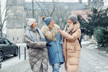 Three cheerful young adult women friend walk Magdeburg street old european uk german town city street enjoy having fun laughing cold winter day together. Female persons friendship celebration weekend
