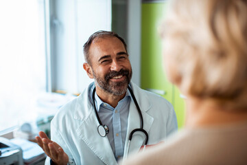 Smiling senior doctor talking to female patient during medical consultation in clinic