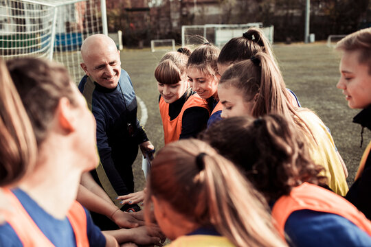 Female youth soccer team forming a huddle on the field with coach