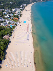 Aerial view of Albena resort on the Bulgarian Black Sea coast with wide sandy beach, umbrellas, hotels and forested hills in summer