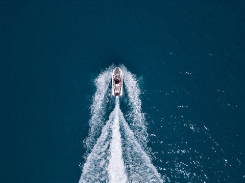 Aerial view of a jet ski speeding across dark blue water, leaving a dynamic white trail. Captured by drone from above, showcasing motion, power, and summer fun on the sea