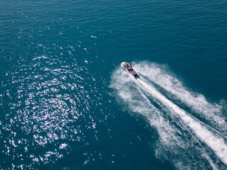 Aerial view of a jet ski speeding across dark blue water, leaving a dynamic white trail. Captured...