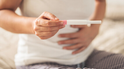 A woman holding a pregnancy test. She is smiling and she is happy about the result