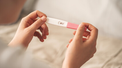 A woman holding a pregnancy test. She is smiling and she is happy about the result