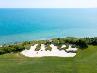 Scenic aerial view of a coastal golf course with green fairways, sand bunkers, golf carts, and...