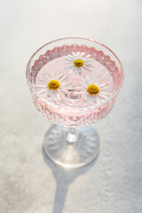 A crystal glass filled with a rose sparkling wine, garnished with floating daisy flowers. Minimalistic creative concept, creating a summery party atmosphere. Refreshing beverages, low alcohol drinks