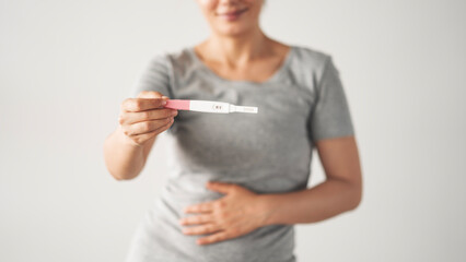 A woman holding a pregnancy test. She is smiling and she is happy about the result