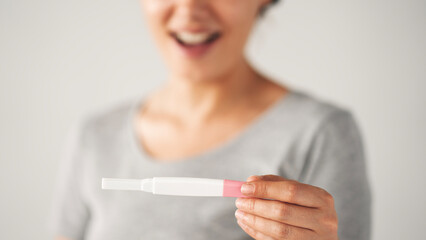 A woman holding a pregnancy test. She is smiling and she is happy about the result