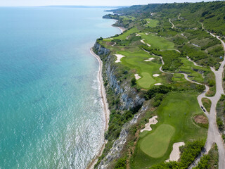 Scenic aerial view of a coastal golf course with green fairways, sand bunkers, golf carts, and...