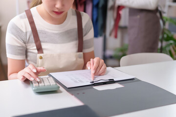 Young Asian Woman Calculating Financial Data on Documents with Calculator for Business Accounting...