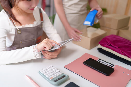 Asian Young Women Using Tablet for Online Business at Home with Packing Parcel Box and Stationery E-commerce Business Concept