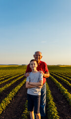 Portrait of senior farmer with his grandson standing in green soybean field and looking at camera.