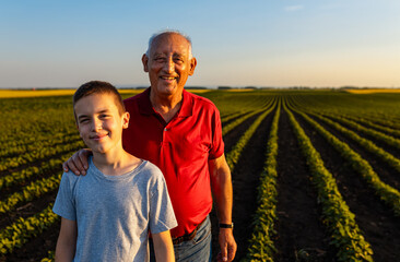 Portrait of senior farmer with his grandson standing in green soybean field and looking at camera.