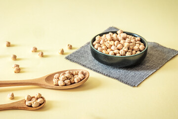 Dry chickpeas in rustic black bowl and wooden spoons on warm beige table. Cozy and natural food flat lay
