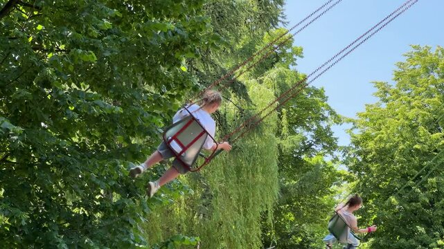 Summer adventure at the fair: Youngsters on a classic chain carousel, feeling the joy of flying.Low angle view of children having fun on a spinning wave swinger, soaring through the air in a park