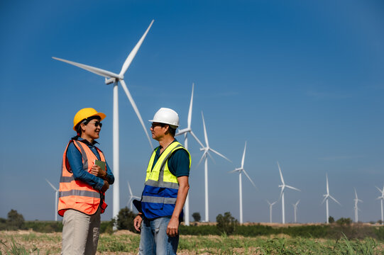 Japanese male wind turbine engineer discussing with Asian technician woman working together in outdoor windmill power plant 