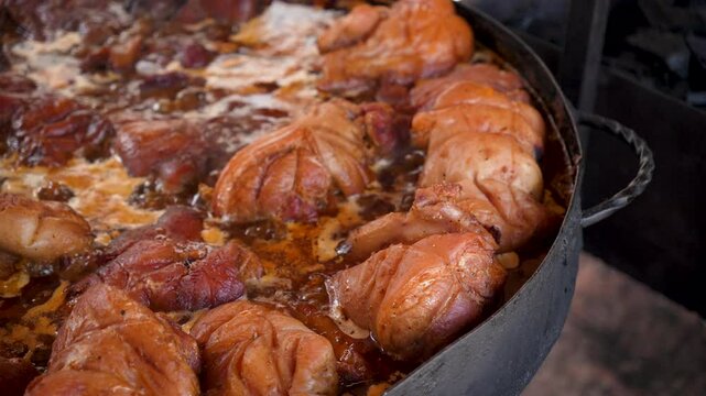 Close-up footage of delicious roasted pork knuckles, a classic German or Czech dish, prepared in a big pan. A popular comfort food at a street fair.Appetizing pork knuckles. Traditional outdoor cookin
