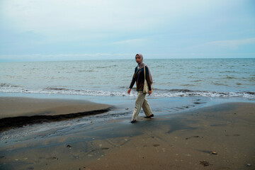 Javanese women wearing hijab walking on the beach, Asian Muslim women walking on the beach with small waves crashing and empty sky for advertising space.