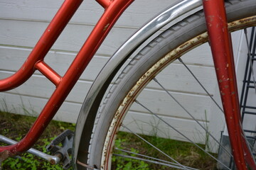 An old red metal bicycle stands against a white fence, on a green lawn. The bicycle parts are old,...