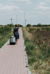 An elderly woman with a suitcase goes to the bus stop.