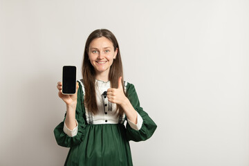 A woman wearing a vibrant green dress stands against a plain background, smiling while holding up a...