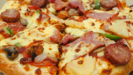 Close-up of a supreme pizza loaded with cheese, sausage, ham, pepperoni, mushrooms, green bell peppers, and pineapple chunks.