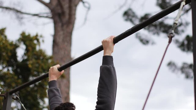 man in a sports hoodie performing dips on a horizontal bar at outdoor fitness park, demonstrating strength, workout, and bodyweight training.