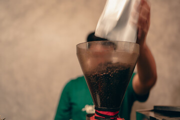 Barista pours coffee beans into the coffee machine tank for grinding standing behind counter. Close...
