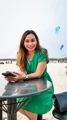 A beautiful woman in a green dress was sitting on a chair with a high table. This is an outdoor cafe on the beach.