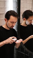 Young man applying shaving foam to cheeks while looking in mirror
