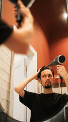 Young man drying hair with a hairdryer in bathroom