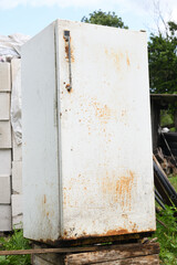 Old rusted refrigerator standing on a wooden pallet in a rural setting