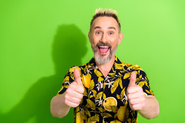 Smiling fashionable man with golden blond mohawk wearing tropical print shirt on vibrant green background