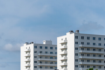 Modern residential buildings with clean lines and white facades rise into the sky. The sky is slightly cloudy.
