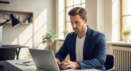 Man Working on Laptop in Modern Office - A focused businessman works on his laptop in a bright, modern office space. Sunlight streams through large windows