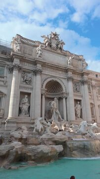 The majestic Trevi Fountain in Rome, Italy, its intricate sculptures and flowing water captivate tourists under a picturesque sky with scattered clouds